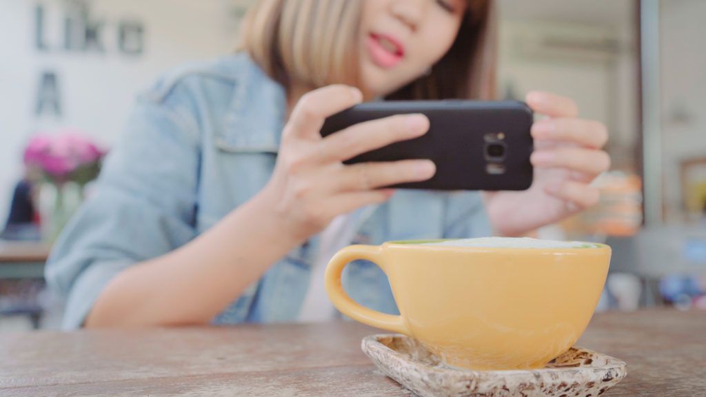 Female blogger photographing green tea cup in cafe with her phone. A young woman taking photo of coffee tea on smartphone, photographing meal with mobile camera.