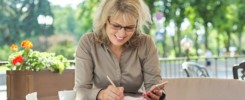 Business beautiful woman writing in business notebook using smartphone