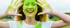 cheerful woman with closed eyes and green holi paint on hands gesturing and smiling outdoors