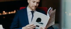 Concentrated businessman looks attentively in menu while sits in cozy restaurant, drinks coffee