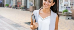 Confident young woman laughing and carrying notepad in hand while standing