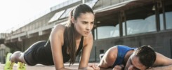 Determined woman doing a plank next to a fatigued man on a track field