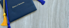 Flat lay of a Diploma of Graduation with honor cords on a simple wooden background.