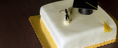 Graduation white cake with cap on the top and diploma decor.