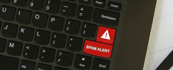 Laptop on workspace area with cyber security red keyboard key with Spam Alert warning written on it