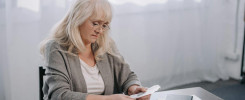 senior woman sitting at table with paperwork and counting money