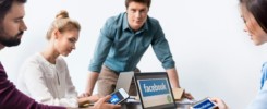 Young businesspeople using digital devices with facebook logo icons on screens