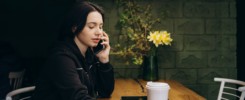 Young charming woman calling with cell telephone while sitting alone in coffee shop during free time