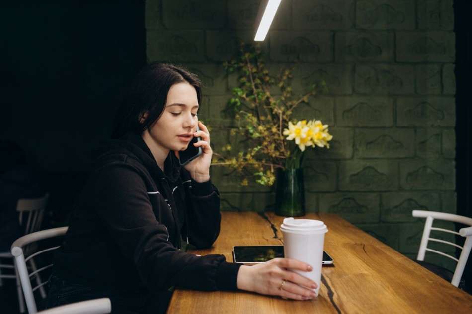 Young charming woman calling with cell telephone while sitting alone in coffee shop during free time