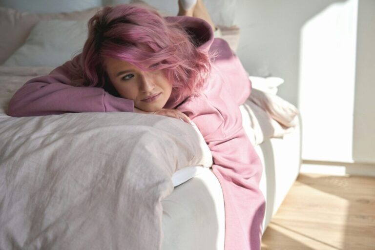 Introvertált vagy extrovertált marketing-tanácsadó? Depressed pensive teen girl introvert pink hair lying on bed looking away.