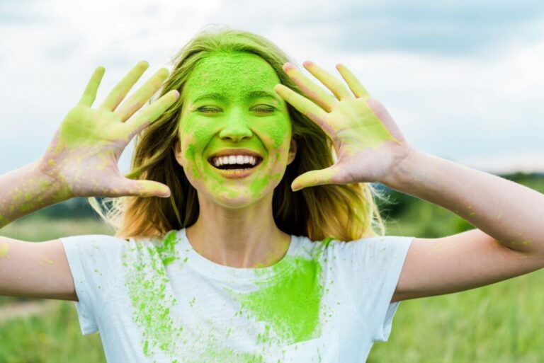A temperamentum szerepe a marketingben cheerful woman with closed eyes and green holi paint on hands gesturing and smiling outdoors