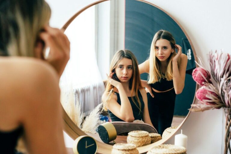 Facebook és nárcizmus – személyiségjegyek és közösségi média Two beautiful teenage girls look at their reflection in the mirror. Young narcissistic women.