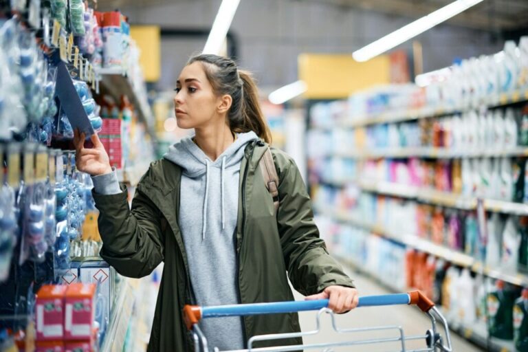 A fogyasztók árészlelésének hatásai Young woman looking at price tag of hygiene products in supermarket.