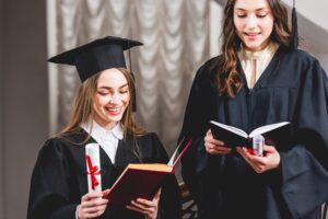 beautiful girls in graduation caps reading books and holding diplomas