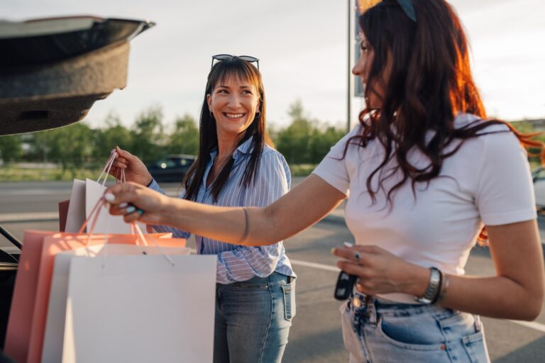 Attribúciós folyamatok a fogyasztói magatartásban Cheerful trendy female buyers putting shopping bags into a car trunk.