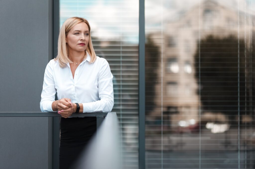Beautiful blonde secretary stands sad near office windows