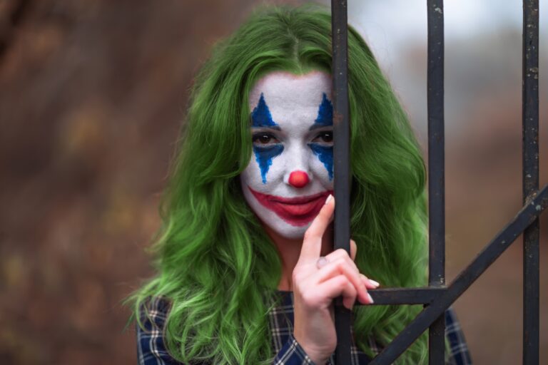 A vállalati pszichopátia Close-up portrait of a greenhaired girl in chekered dress with joker makeup on a blurry background.