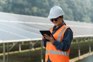 Female electrical engineer using laptop to check solar panel farm equipment, eco-friendly energy