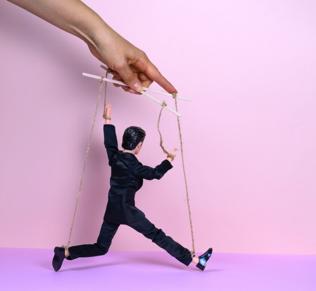 female hand with a puppet of a man in a black business suit on a pink background