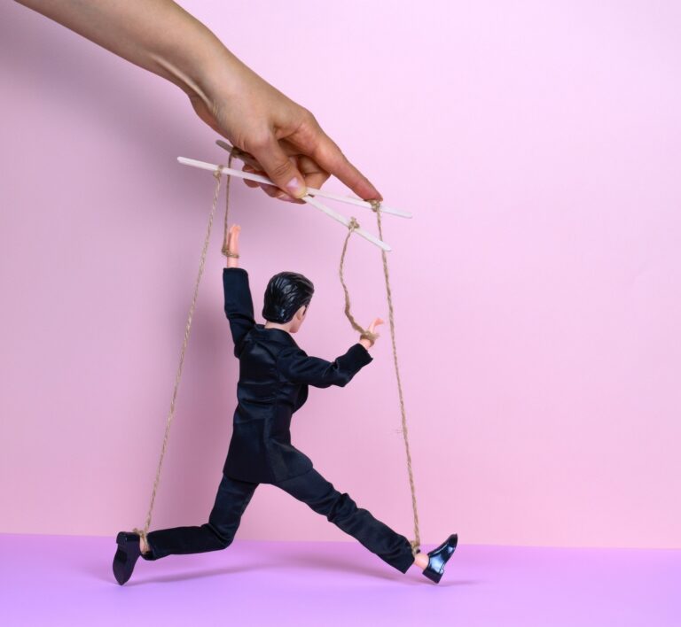 female hand with a puppet of a man in a black business suit on a pink background