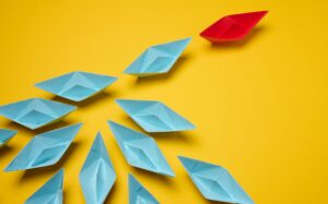 Group of blue paper boats following on red on yellow background, mass manipulation