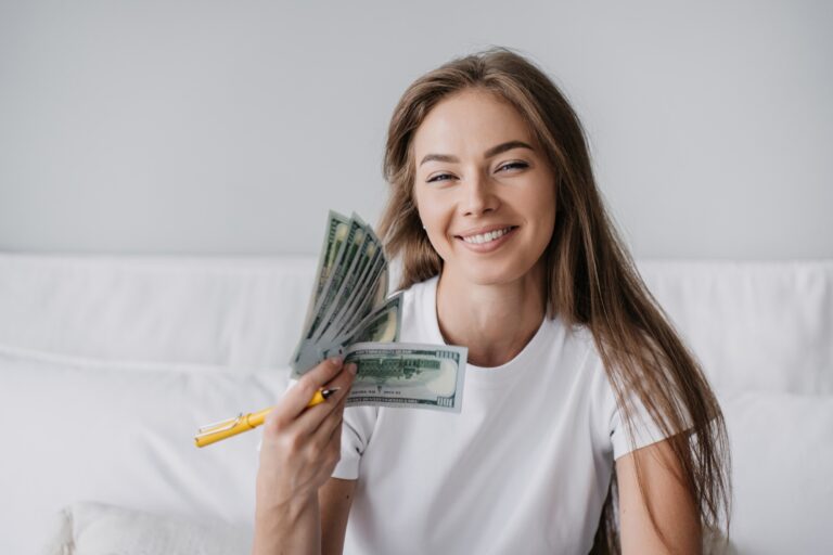 Happy girl in white t-shirt smiles holds dollar banknotes using mine like fan, satisfied by wage