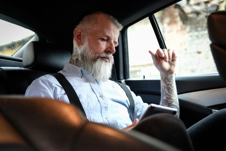 Old man businessman with tablet inside car in daytime
