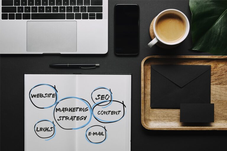 A marketing alapjai: útmutató kezdőknek Open notebook with"marketing strategy" icons by stationery and laptop on black background