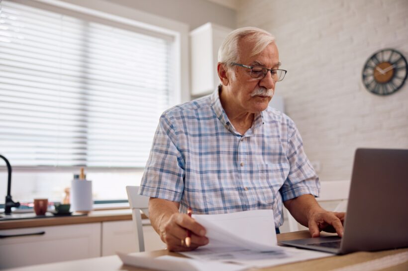 Befektetési stratégiák a világgazdaság új korszakában Senior man using laptop while analyzing financial bills at home.
